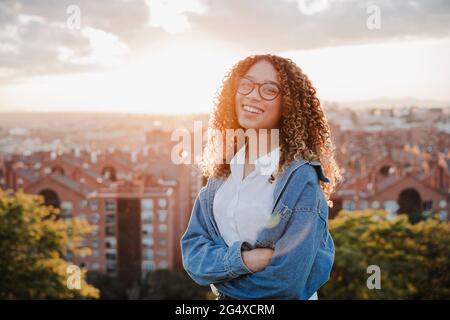 Glückliche Frau mit gekreuzten Armen vor der Stadt bei Sonnenuntergang Stockfoto