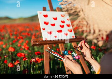 Künstlerin mit Farbe auf Palette für Leinwand auf dem Mohn-Feld Stockfoto