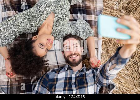 Lächelnder Mann, der mit der Frau über das Mobiltelefon Selfie gemacht hat, während er auf der Decke liegt Stockfoto