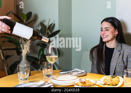 Der männliche Kellner serviert Getränke in Weinglas von einer lächelnden Geschäftsfrau im Restaurant Stockfoto