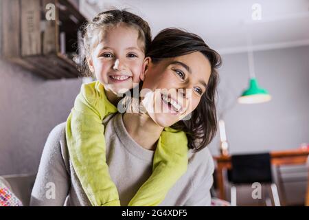 Lächelnde Mutter Huckepack Tochter zu Hause Stockfoto