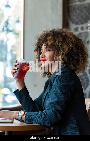 Geschäftsfrau schaut weg, während sie Eiskaffee im Café hält Stockfoto