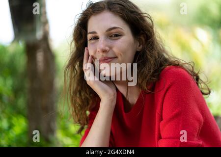 Lächelnde Frau mit der Hand am Kinn im Garten Stockfoto