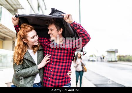 Ein Paar, das bei Regen unter einer Jacke auf der Straße läuft Stockfoto