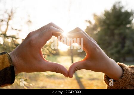 Die Hände von Mann und Frau bilden während des Sonnenuntergangs ein Symbol für die Herzform Stockfoto