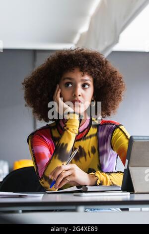 Nachdenkliche Universitätsstudentin mit Hand am Kinn, die in der Bibliothek wegschaut Stockfoto