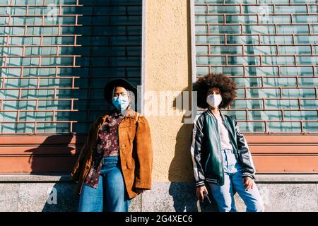 Junge Frauen mit schützenden Gesichtsmasken stehen mit sozialer Distanz vor dem Gebäude Stockfoto