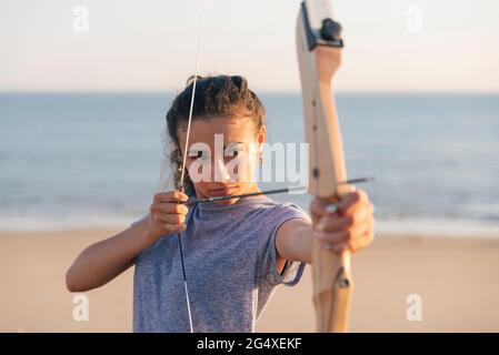 Junge Frau übt Bogenschießen am Strand Stockfoto