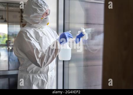 Hygienearbeiterin sprüht Chemikalien auf Glas, während sie das Bürogebäude desinfiziert Stockfoto
