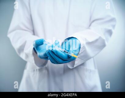 Ärztin mit Labormantel und Schutzhandschuh mit COVID-19-Impfstoffspritze Stockfoto