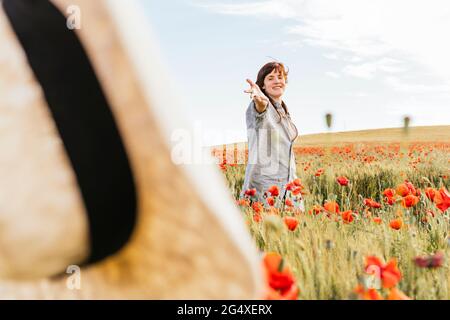 Lächelnde Frau, die einen Hut wirft, der im Mohnfeld steht Stockfoto
