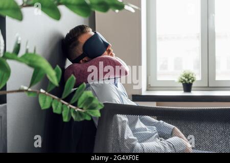 Erschöpfter Geschäftsmann mit Augenmaske und Nackenkissen, der im Büro schläft Stockfoto