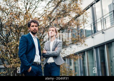 Geschäftsfrau mit gekreuzten Armen, die von einem Kollegen im Büropark steht Stockfoto