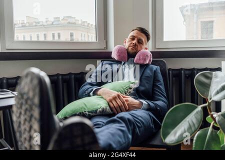 Geschäftsmann mit Nackenkissen, der sich im Büro auf einem Stuhl entspannen kann Stockfoto