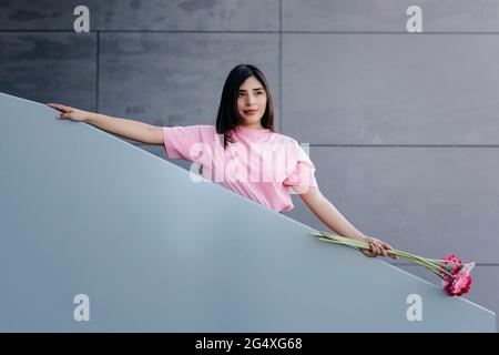 Schöne Frau mit Blumen, die vor einer grauen Wand am Geländer stehen Stockfoto