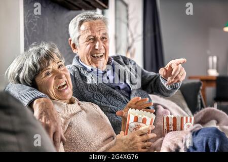 Seniorenpaar sitzt zu Hause mit Popcorn auf dem Sofa Stockfoto