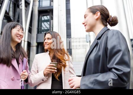 Unternehmerinnen mit Kaffeetasse und Akte diskutieren im Stehen miteinander Stockfoto