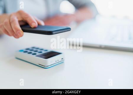 Geschäftsfrau scannt QR-Code auf dem Mobiltelefon über das Kartenterminal am Schreibtisch Stockfoto