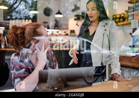 Eine Schwangere mit der Hand auf dem Bauch spricht mit einer Freundin im Café Stockfoto