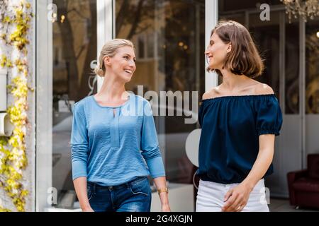 Lächelnde Geschäftsfrauen, die sich beim Gehen vor dem Büro gegenseitig anblicken Stockfoto