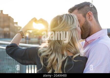 Ein romantisches Paar küsst sich gegenseitig, während es mit den Händen Herzform macht Stockfoto
