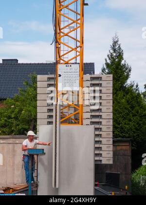 Ein Bauarbeiter vor einem Kran, der das Heben eines vorgefertigten Bauteils unterstützt Stockfoto