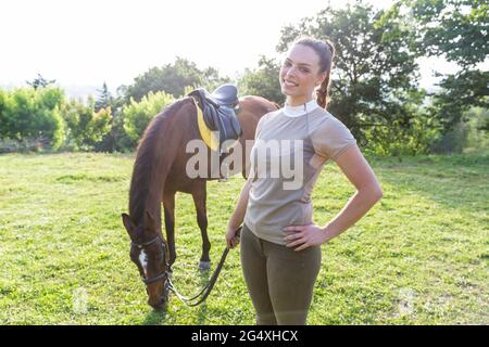 Lächelnde Frau, die die Zügelung hielt, während sie auf der Ranch neben dem Pferd stand Stockfoto