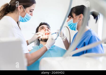 Zahnärztinnen, die während einer Pandemie Zahnbohrungen bei männlichen Patienten in der Klinik durchführen Stockfoto