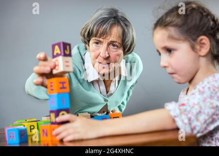 Ältere Frau stapelt Spielzeugblock, während sie mit Mädchen zu Hause spielt Stockfoto