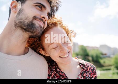 Lächelnde Freundin, die sich an sonnigen Tagen auf die Schulter eines Freundes lehnt Stockfoto