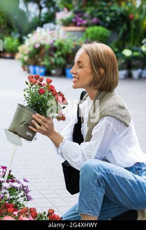 Lächelnde Frau riecht Blumen, während sie auf dem Fußweg hockend ist Stockfoto