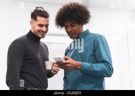 Männliche Fachleute, die im Büro auf das Smartphone schauen Stockfoto