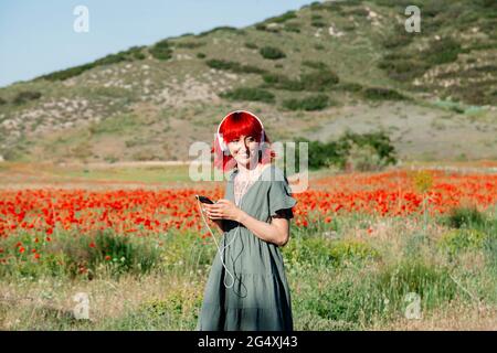 Junge rothaarige Frau, die Musik auf dem Mohnfeld hört Stockfoto