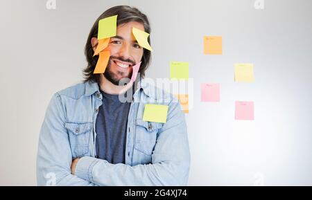 Lächelnder, professioneller Mann, der mit Haftnotizen auf dem Gesicht steht Stockfoto