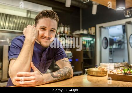 Lächelnder Barkeeper, der auf der Theke gelehnt steht Stockfoto