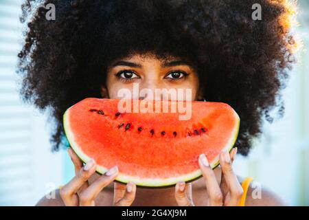 Afro-Frau bedeckt das Gesicht mit einer Scheibe Wassermelone Stockfoto