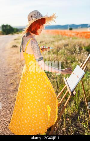 Weibliche Künstlerin Malerei auf Leinwand auf dem Feld an sonnigen Tag Stockfoto