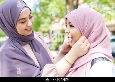 Schöne Frau, die Hijab einer Freundin im öffentlichen Park anpasst Stockfoto