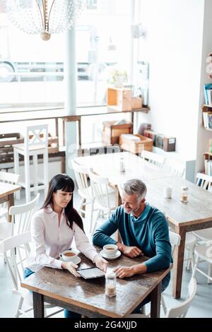 Männliche und weibliche Besitzer, die im Café ein digitales Tablet benutzen Stockfoto