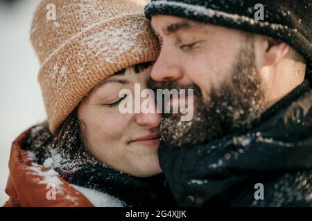 Lächelnde Freundin trägt Strickmütze umarmt Freund Stockfoto