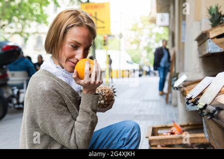 Frau riecht Obst, während sie auf dem Straßenmarkt hocken Stockfoto