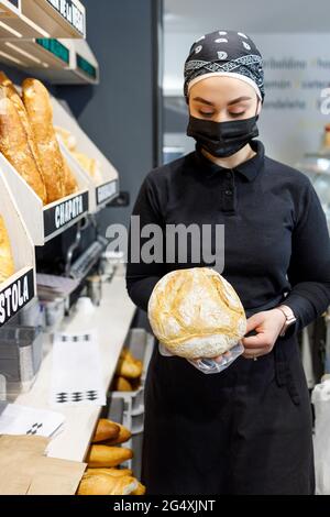 Weibliche Bäckerin, die während einer Pandemie Brot in der Bäckerei hält Stockfoto