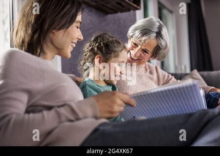 Tochter schaut sich das Fotoalbum an, während sie bei der Familie im Wohnzimmer sitzt Stockfoto