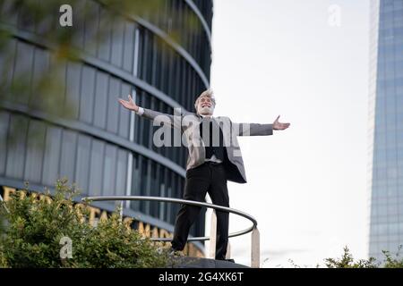 Ekstatischer Geschäftsmann mit ausgestreckten Armen, der vor dem Bürogebäude steht Stockfoto