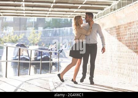 Liebevolles Paar, das sich umarmt, während es auf dem Fußweg unter der Brücke steht Stockfoto