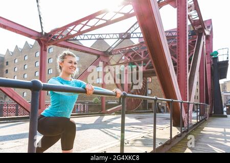 Junge Frau streckt sich, während sie sich auf das Geländer stützt Stockfoto