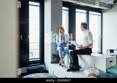 Männliche und weibliche Fachleute diskutieren, während sie auf Möbeln im Büro sitzen Stockfoto