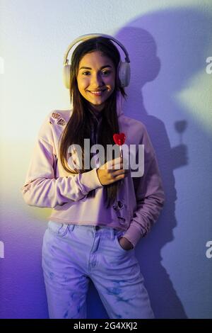Lächelnde Frau mit Lutscher, während sie vor der Wand Musik hört Stockfoto