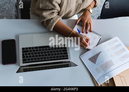 Geschäftsfrau, die im Büro an Finanzdaten arbeitet und Tagebuch schreibt Stockfoto