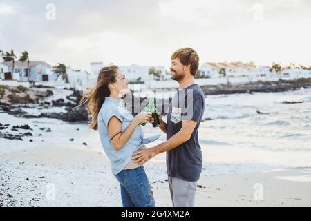 Ein Paar mit mittleren Erwachsenen, das am Strand steht und Getränke anrösten kann Stockfoto